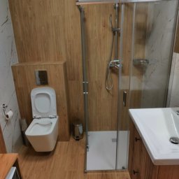 Tobiasz Madoń - Nowoczesna łazienka z kabiną prysznicową, toaletą i umywalką w drewnianej zabudowie. Ściany wykończone płytkami imitującymi drewno i marmur.