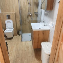 Tobiasz Madoń - Nowoczesna łazienka w odcieniach beżu i bieli: kabina prysznicowa ze szklanymi drzwiami, umywalka z szafką w kolorze drewna i podwieszana toaleta.