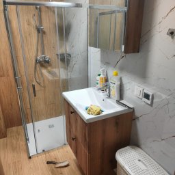 Tobiasz Madoń - Nowoczesna łazienka z kabiną prysznicową typu walk-in, drewnianą szafką pod umywalką i marmurowymi płytkami ściennymi z brązowymi żyłami.