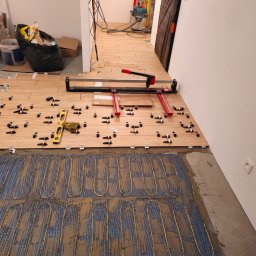 Tobiasz Madoń - Montaż ogrzewania podłogowego i układanie płytek drewnopodobnych. Widoczna poziomica, prasa do cięcia płytek i krzyżyki dystansowe.