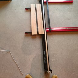 Tobiasz Madoń - Cięcie paneli podłogowych za pomocą gilotyny RedTechnic na szarym betonowym podłożu. Widoczne dwie przycięte deski i fragmenty butów.