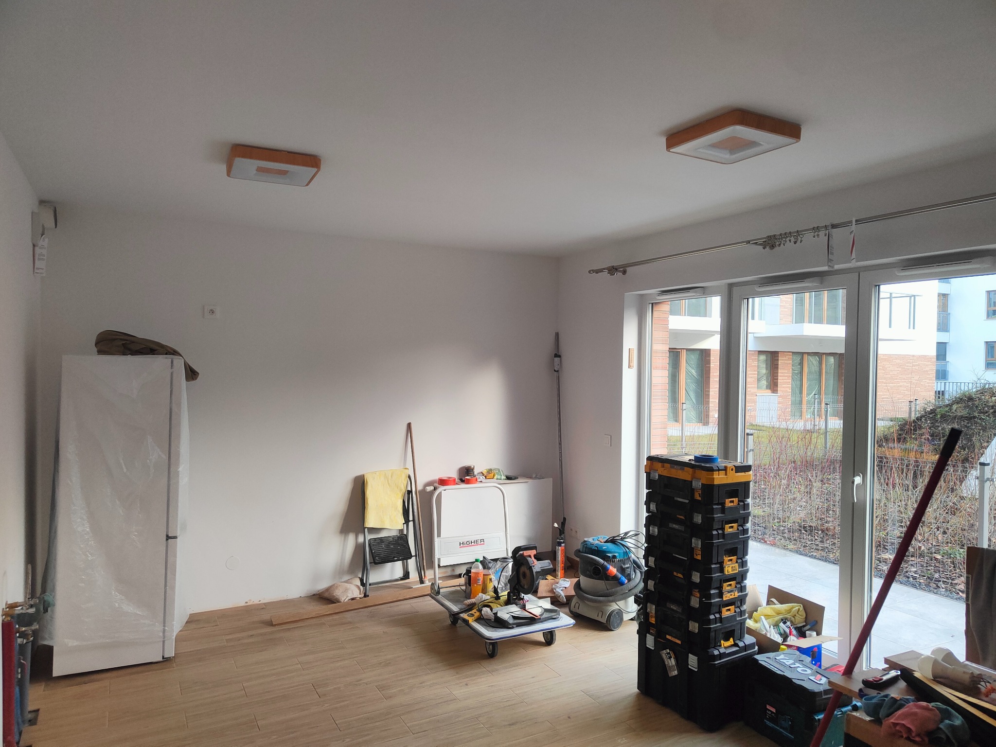 Wnętrze w Huta-Dąbrowa w trakcie prac wykończeniowych: panele na podłodze, narzędzia, drabina, okna balkonowe. Przygotowanie do dalszych prac.