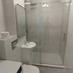REM-TUR - Nowoczesna łazienka z kabiną prysznicową typu walk-in, umywalką nablatową i toaletą. Ściany wykończone marmurkową okładziną. Widoczna pralka w dolnym rogu.
