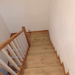REM-TUR - Wykończone schody wewnętrzne z drewnianymi stopniami i białymi balustradami, widok z góry, minimalistyczny design, jasne ściany, naturalne światło.