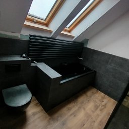 REM-TUR - Nowoczesna, ciemna łazienka na poddaszu z oknem dachowym, drewnianą podłogą i czarną armaturą. Uwagę przykuwa wanna obudowana płytkami w kolorze grafitu.