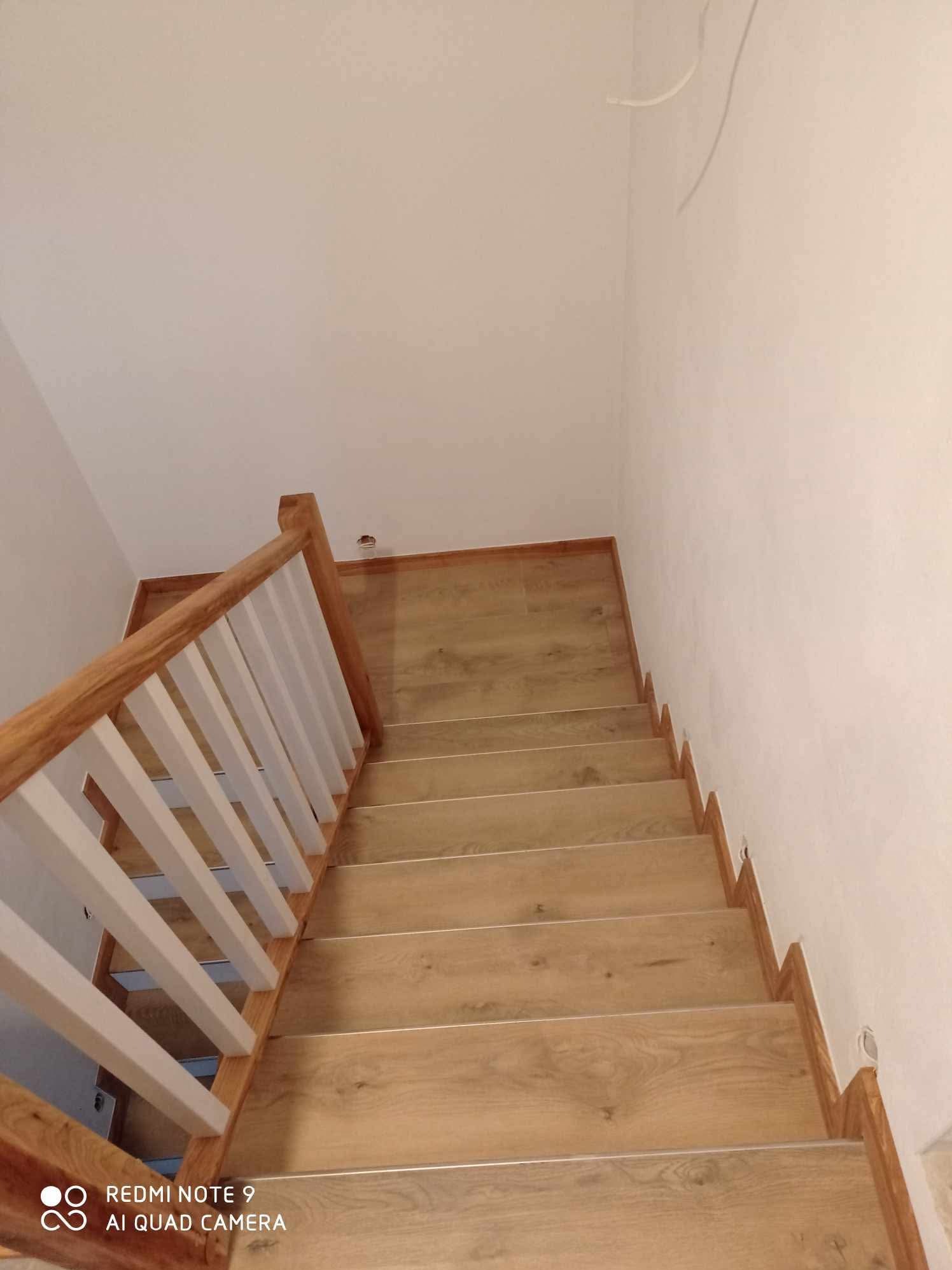 Wykończone schody wewnętrzne z drewnianymi stopniami i białymi balustradami, widok z góry, minimalistyczny design, jasne ściany, naturalne światło.