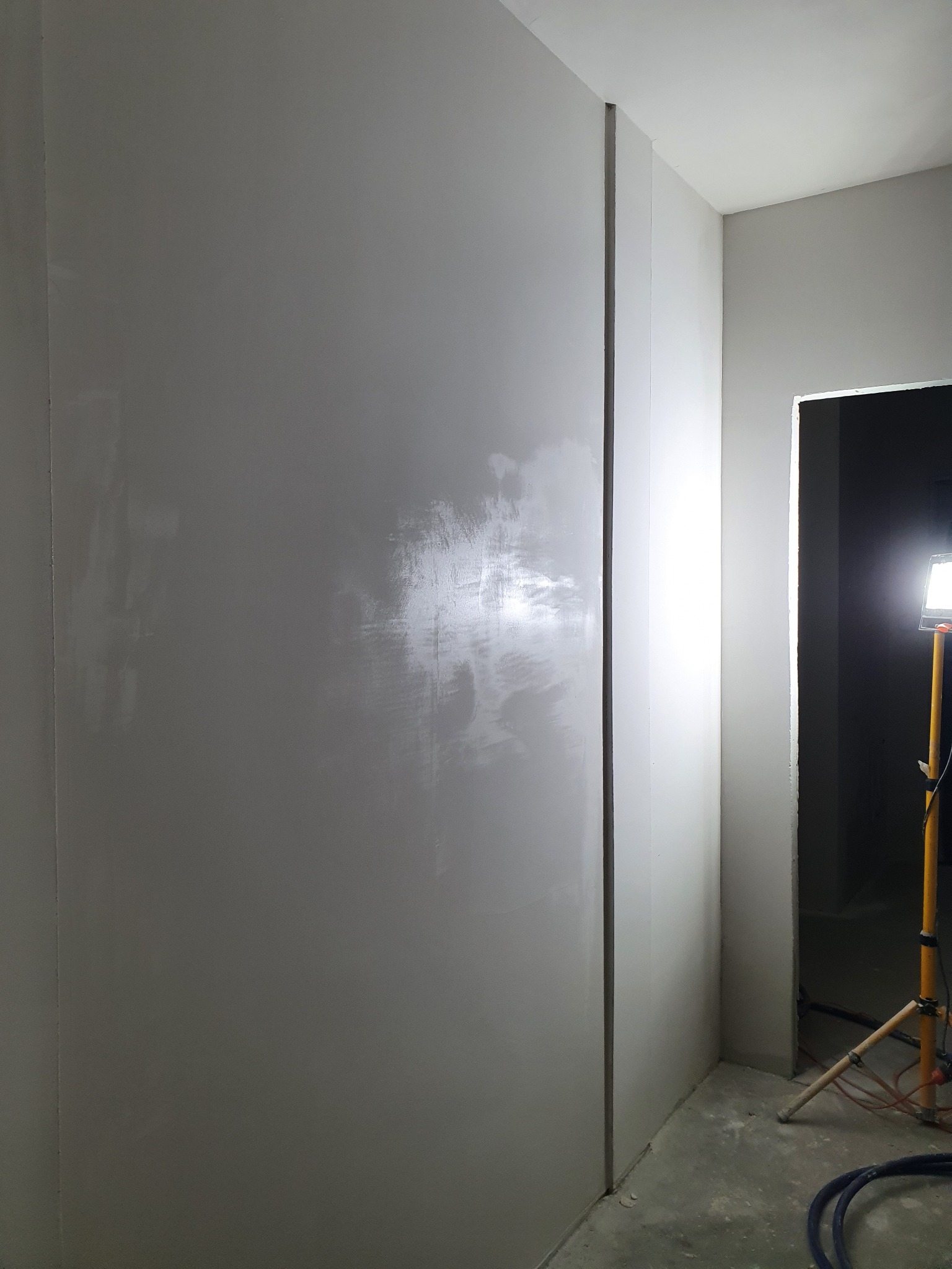 Ściana po nałożeniu gładzi, widoczne ślady szpachlowania pod światłem lampy roboczej