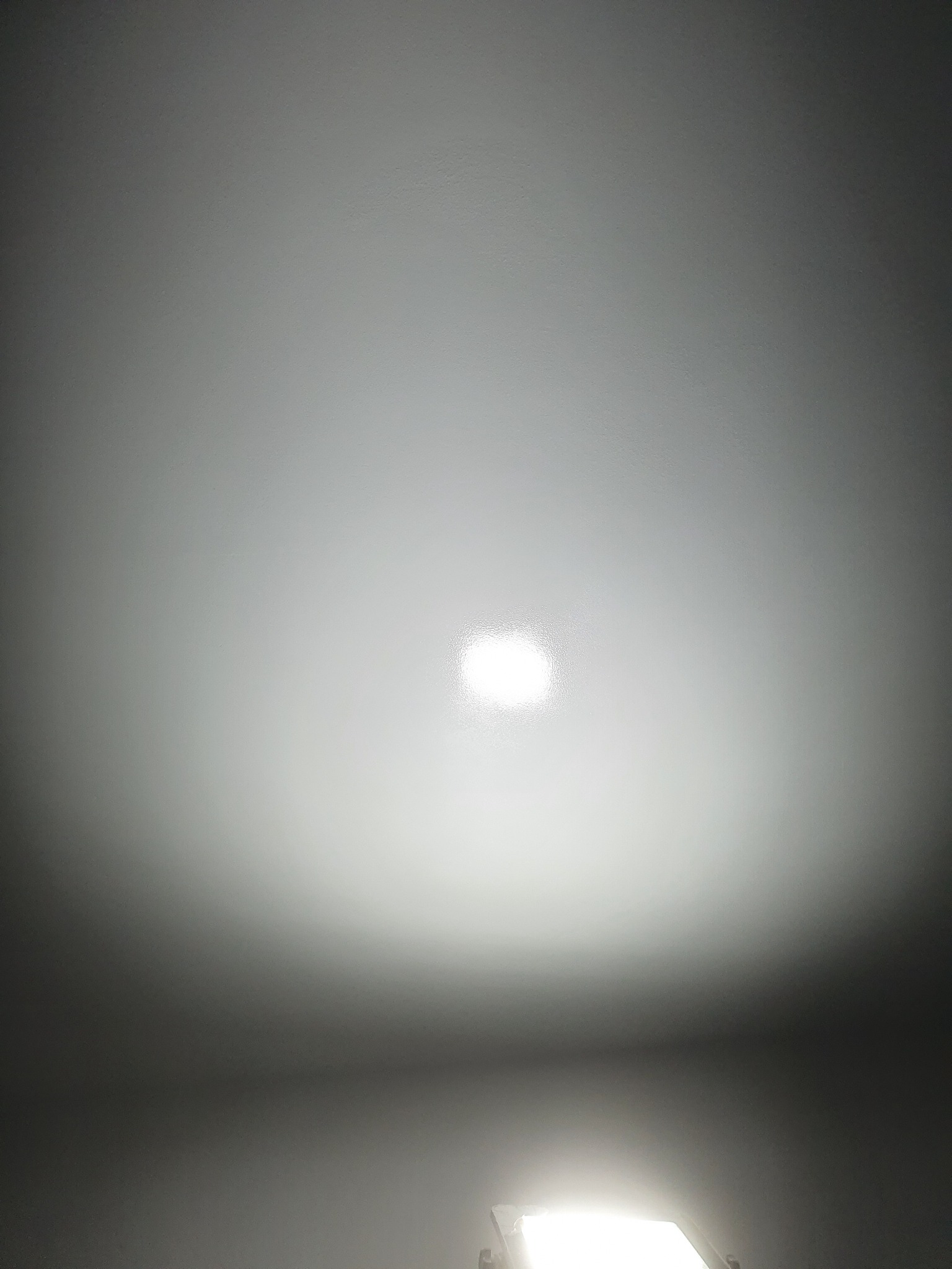 Gładka, pomalowana na biało powierzchnia sufitu z widocznym punktowym oświetleniem centralnym i fragmentem okna w dolnej części kadru.