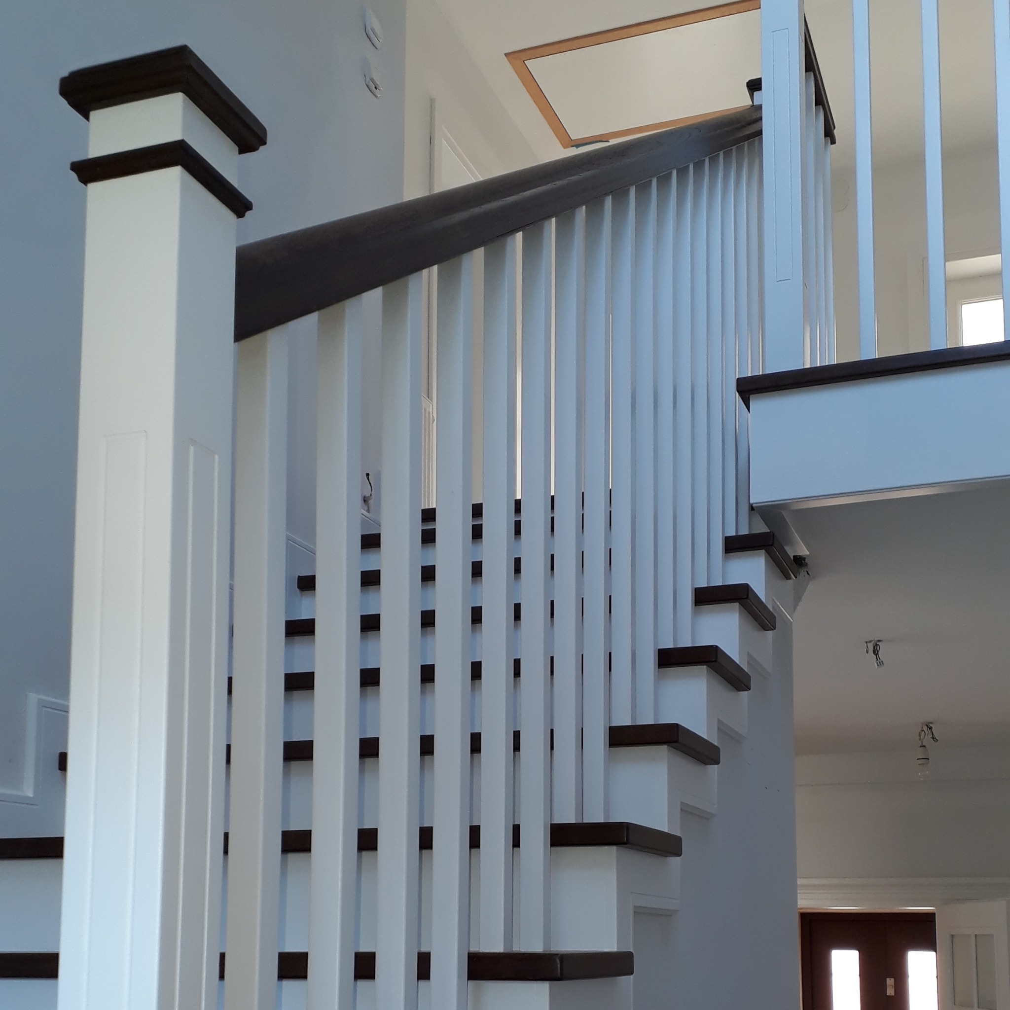 Nowoczesne schody z białymi balustradami i ciemnobrązowymi stopniami, widok z dołu, oświetlenie górne.