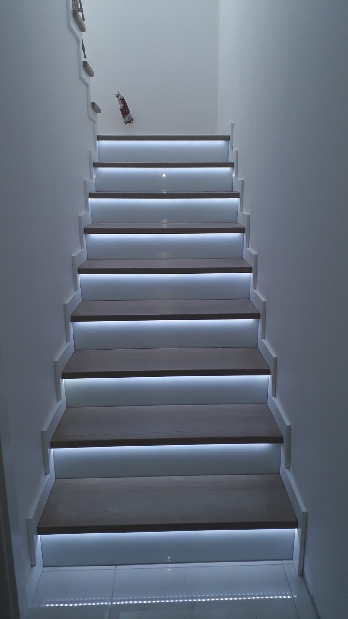 Nowoczesne schody z podświetleniem LED, widok z dołu, białe ściany, minimalistyczny design, na ścianie przyklejony plakat.