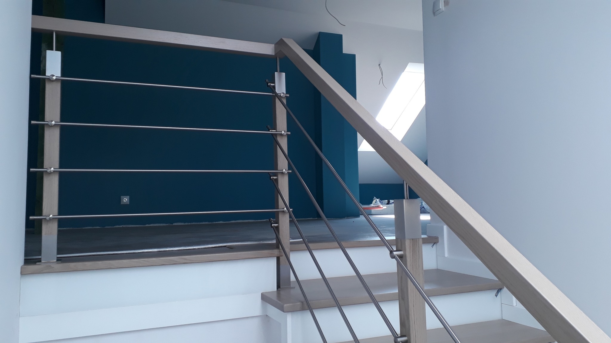 Fragment schodów z drewnianymi stopniami i balustradą z drewnianą ramą i stalowymi linkami w domu w Błażowej, widok z dołu.