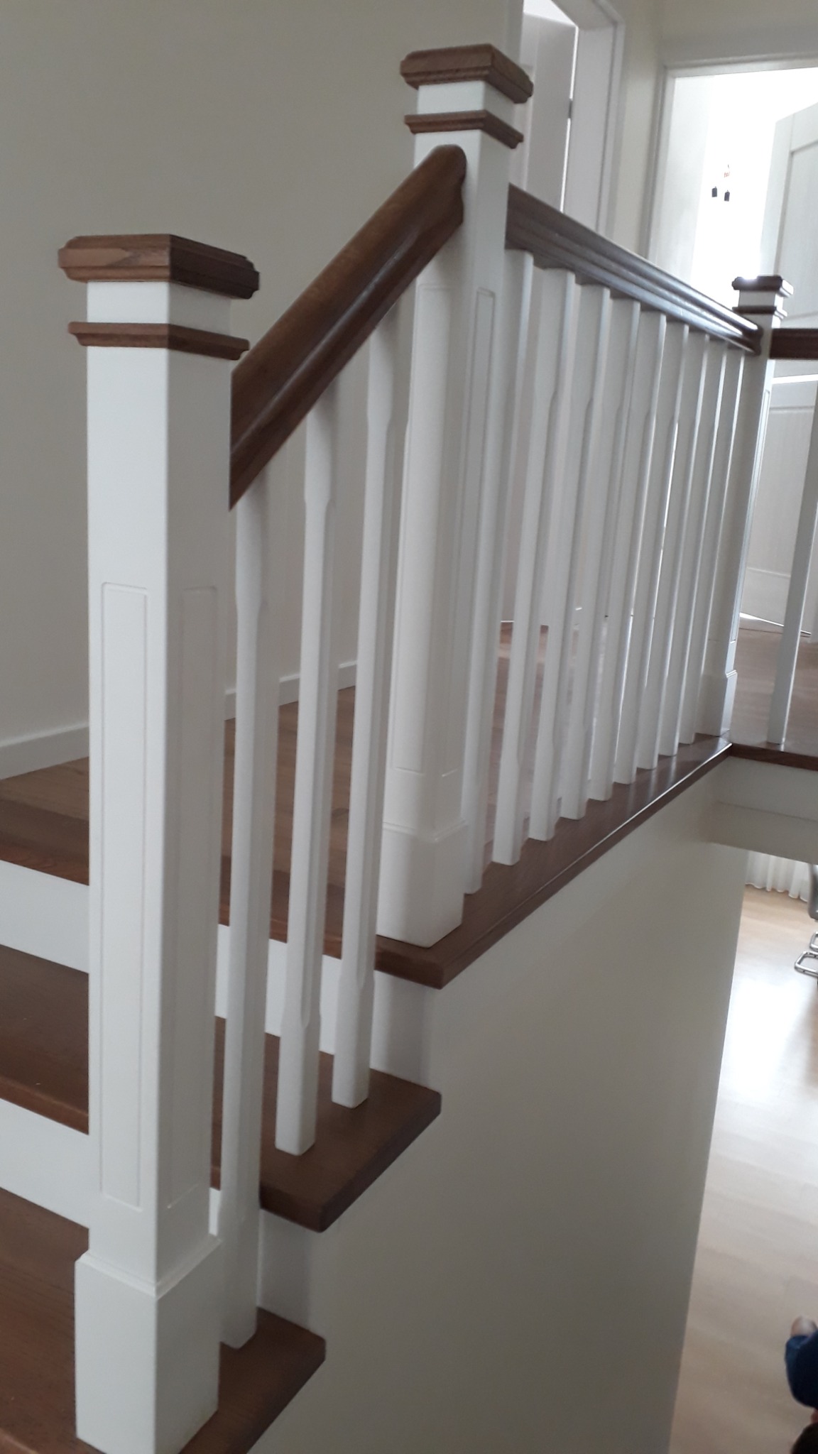 Białe schody z drewnianymi stopniami i balustradą, brązowy drewniany pochwyt, widok z dołu na górę, nowoczesny design.