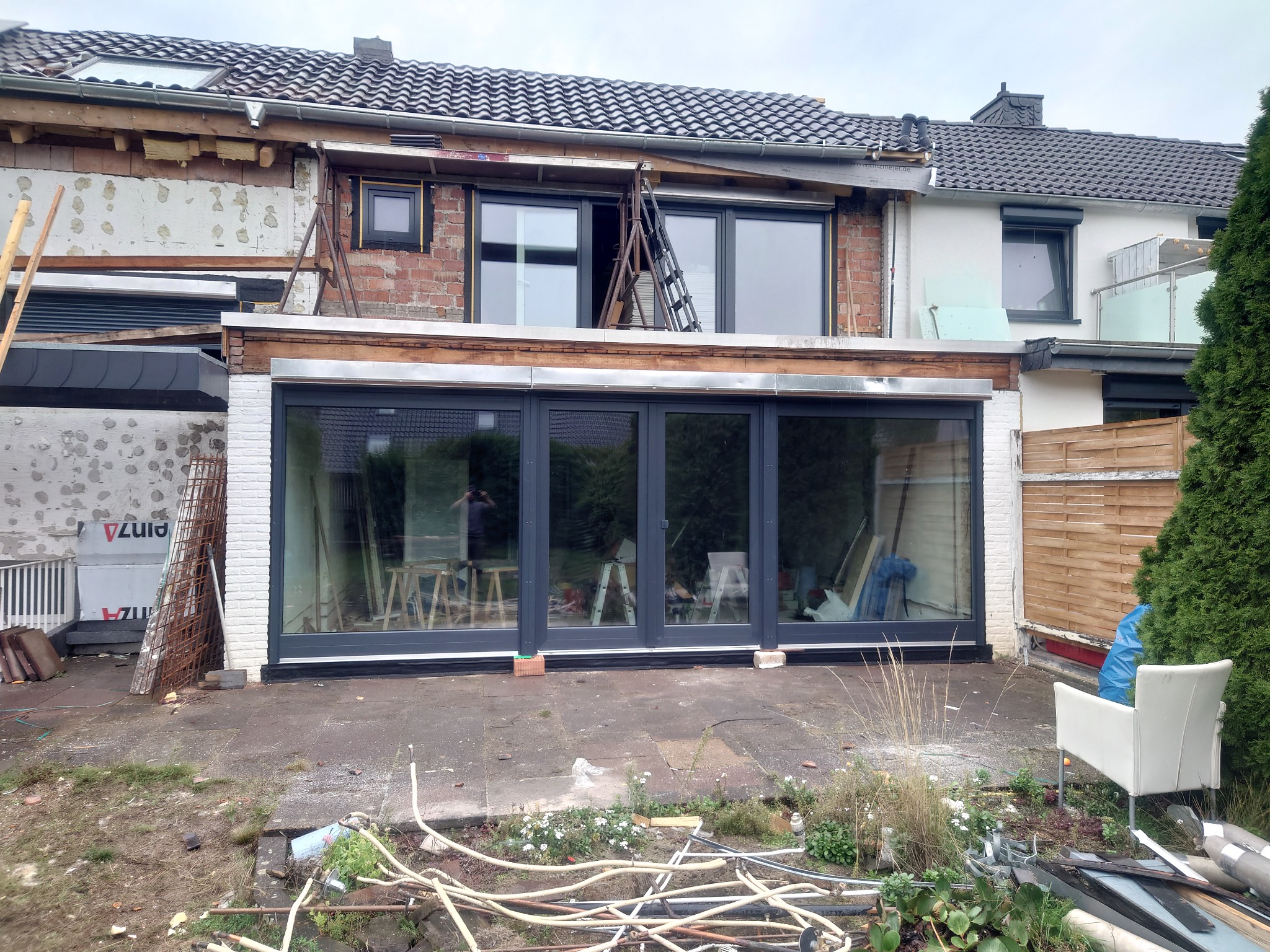 Montaż dużych, przesuwnych okien w Wolsztynie, widok na budynek w trakcie prac wykończeniowych, z widoczną konstrukcją dachu i elewacją w stanie surowym, drabina oparta o okno na wyższej kondygnacji.