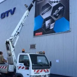 Montaż wielkoformatowej reklamy GTV na elewacji budynku z użyciem podnośnika koszowego.