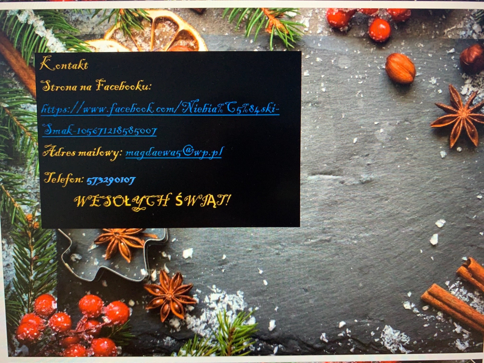 Świąteczna kompozycja z anyżem, cynamonem, gałązkami świerku i owocami na ciemnym tle, częściowo zasłonięta kartką z życzeniami i danymi kontaktowymi.