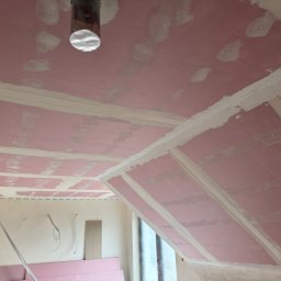 SOBEX TEAM - PATRYK SOBIŚ - Montaż płyt kartonowo-gipsowych na skośnym suficie poddasza. Widoczne łączenia płyt wzmocnione taśmą i wstępnie zaszpachlowane. Elementy instalacji wystają z sufitu.