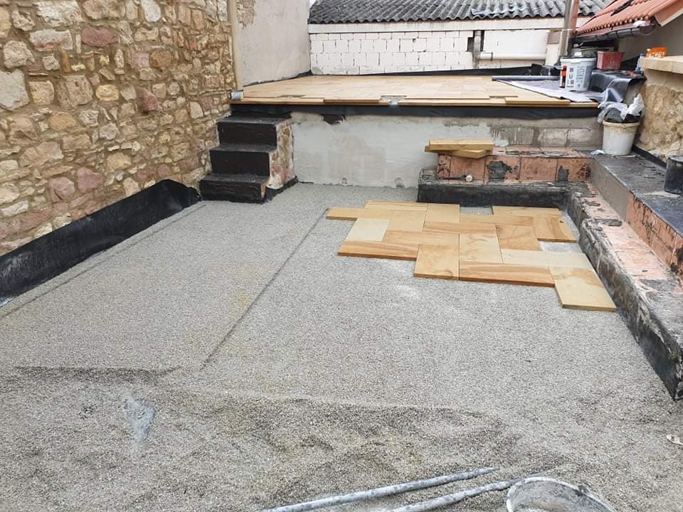 Układanie piaskowych płytek na przygotowanym podłożu z grysu w przestrzeni zewnętrznej, widoczny fragment kamiennej ściany i schody.