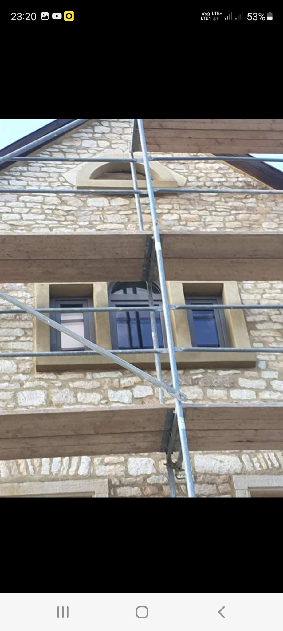 Kamienna elewacja budynku z nowo osadzonymi oknami, widoczne rusztowanie, etap prac wykończeniowych.