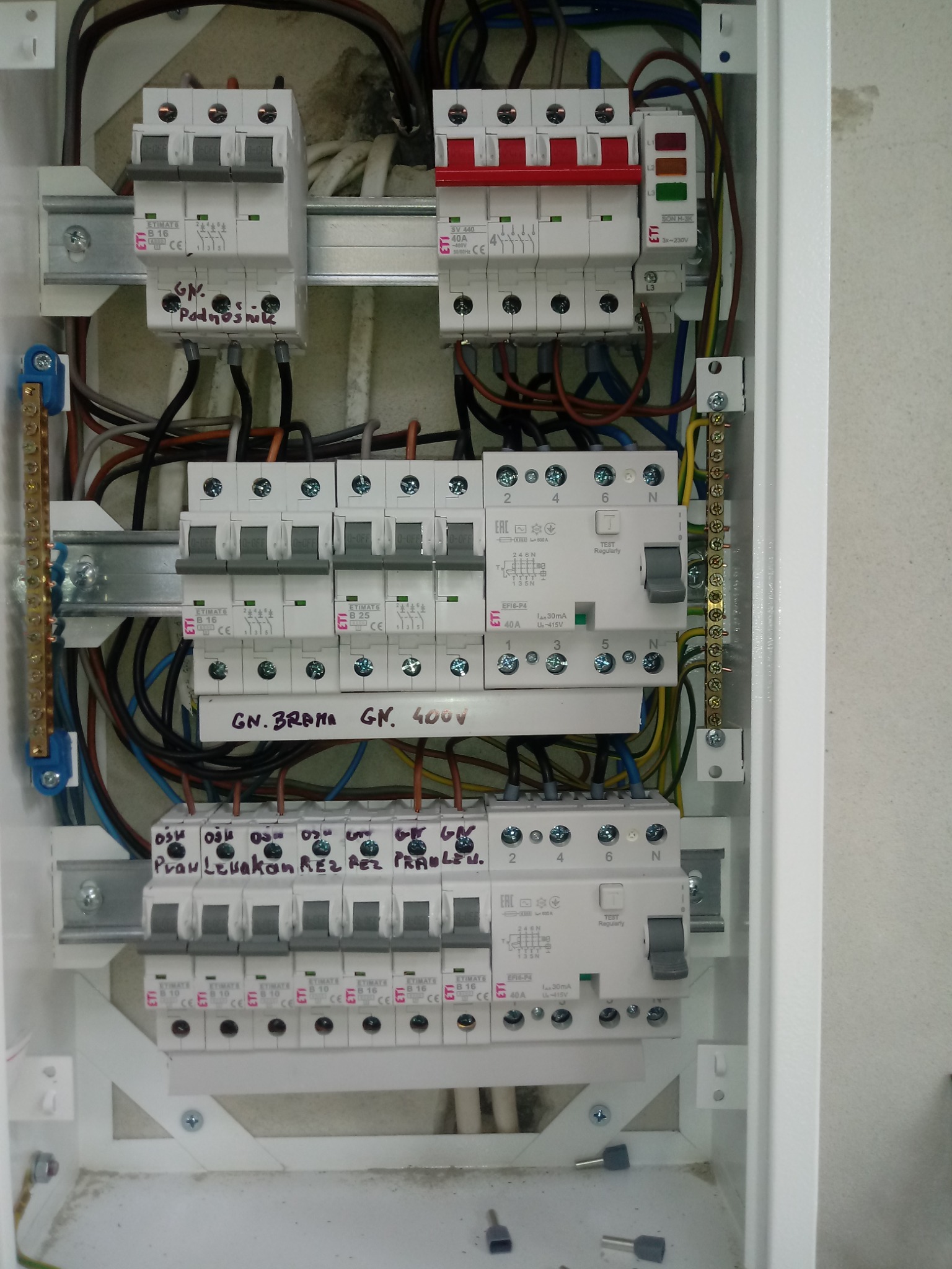 Otwarta skrzynka elektryczna z zainstalowanymi bezpiecznikami i przewodami, widoczne oznaczenia ręczne na obudowie bezpieczników.