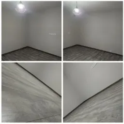 Pusty pokój po remoncie: szare panele podłogowe, białe ściany z gniazdkami elektrycznymi, nowoczesna lampa sufitowa z geometrycznym kloszem.