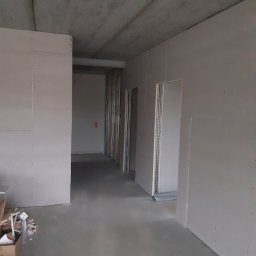 Mop i Szpachelka Sławomir Ramczyk - Surowe wnętrze w trakcie prac wykończeniowych: widoczne płyty gipsowo-kartonowe na ścianach, surowy betonowy strop i metalowe profile konstrukcyjne, przygotowane do dalszych prac.
