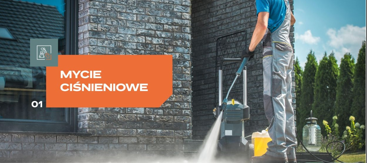 Pracownik w kombinezonie roboczym czyści elewację z szarej cegły za pomocą myjki ciśnieniowej, w tle widoczne zielone tuje.