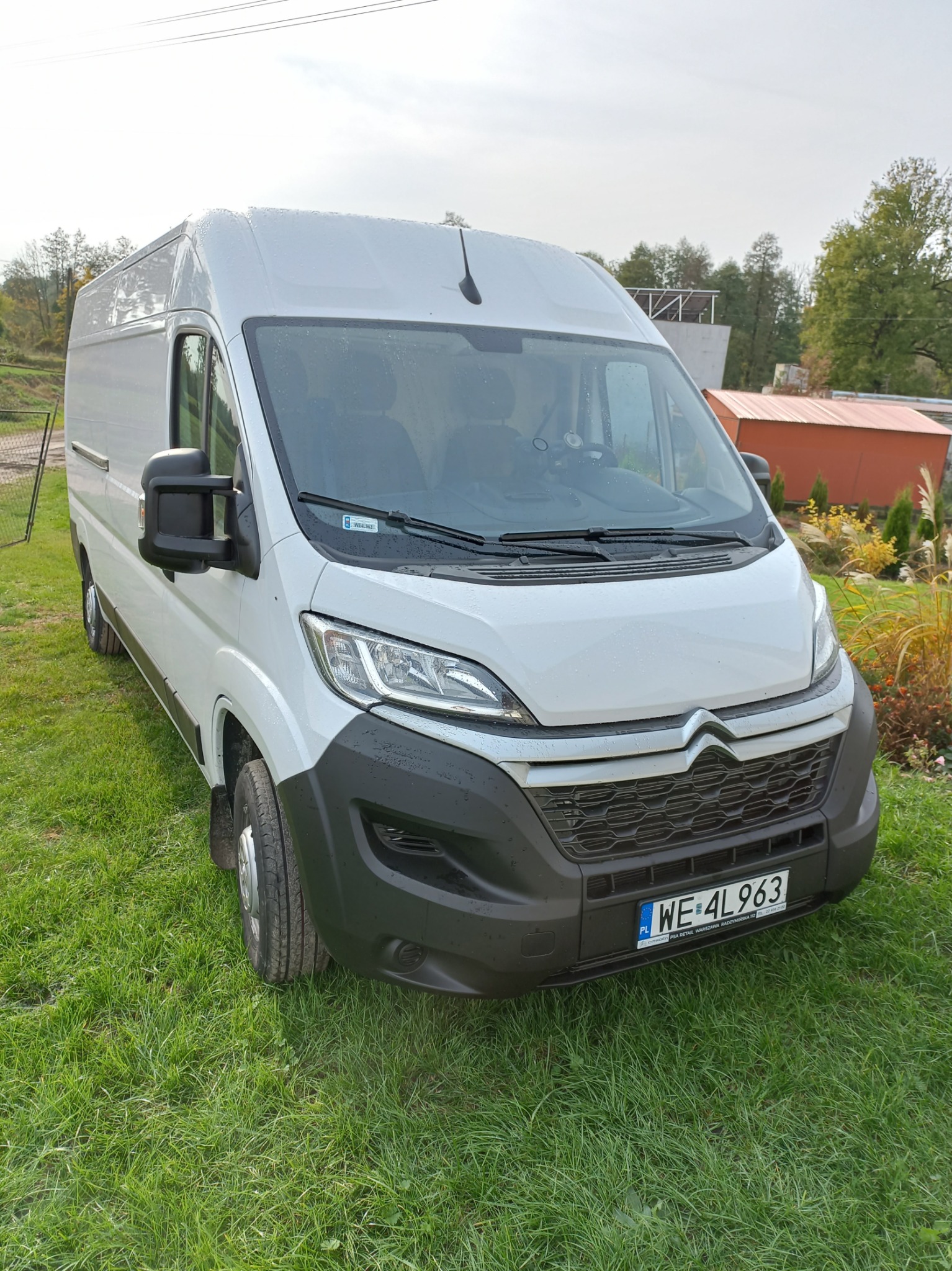 Biały samochód dostawczy Citroen na trawie, z widoczną tablicą rejestracyjną WE 4L963 i kroplami deszczu.