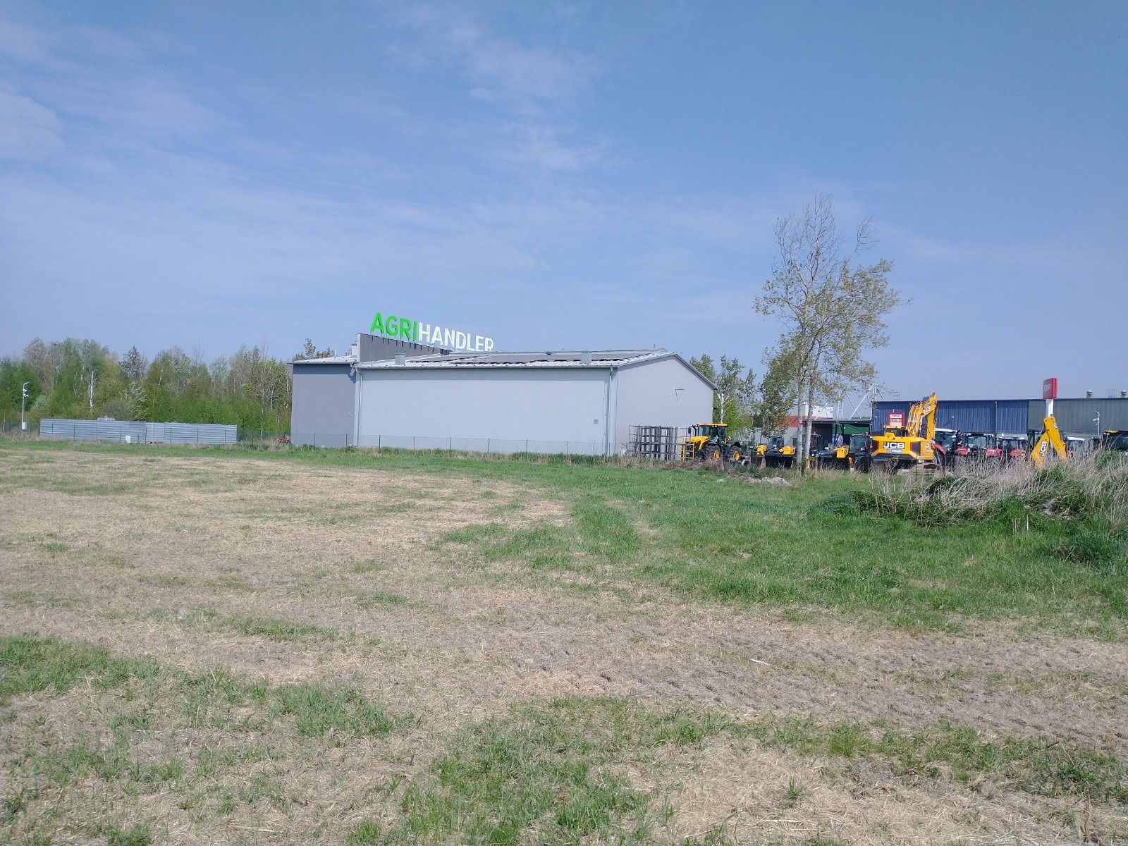 Budynek Agrihandler z panelami fotowoltaicznymi na dachu, w tle maszyny budowlane i rolnicze.