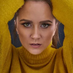 Portret kobiety w żółtym swetrze z golfem, ręce uniesione nad głową, intensywne spojrzenie w obiektyw.