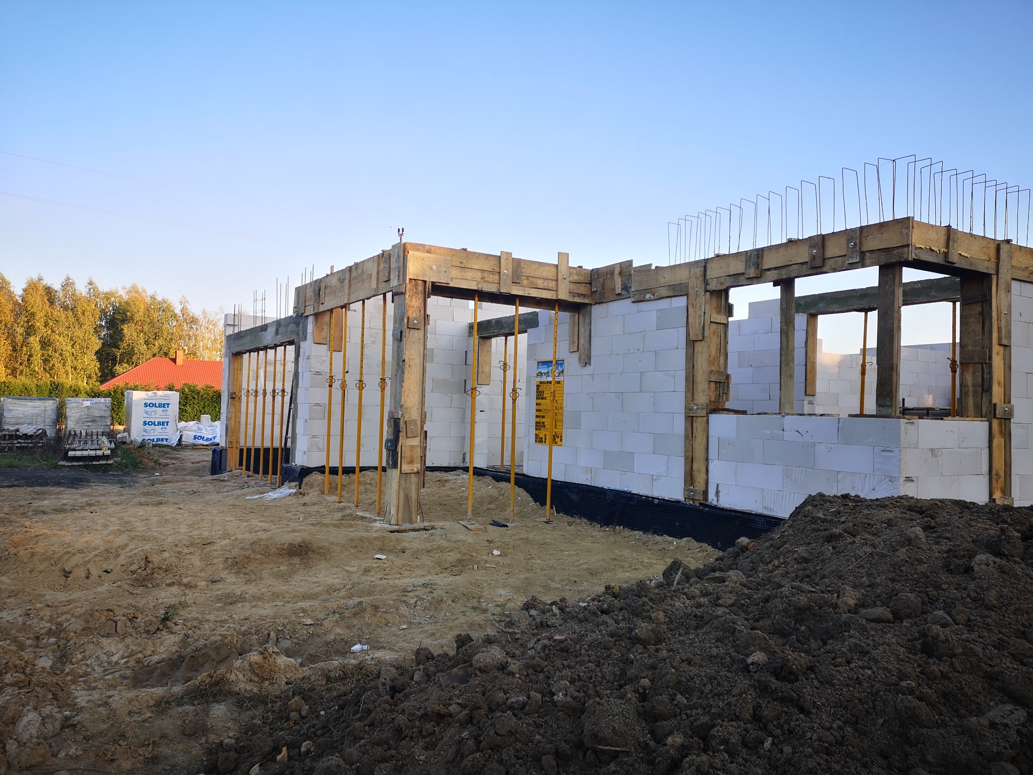 Wznoszenie ścian domu z bloczków betonu komórkowego, widoczne drewniane szalunki i podpory, w tle worki z zaprawą murarską.