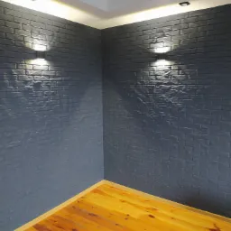 Wnętrze pokoju z pomalowaną na szaro ścianą imitującą cegłę, oświetloną przez dwie lampy ścienne i drewnianą podłogą.