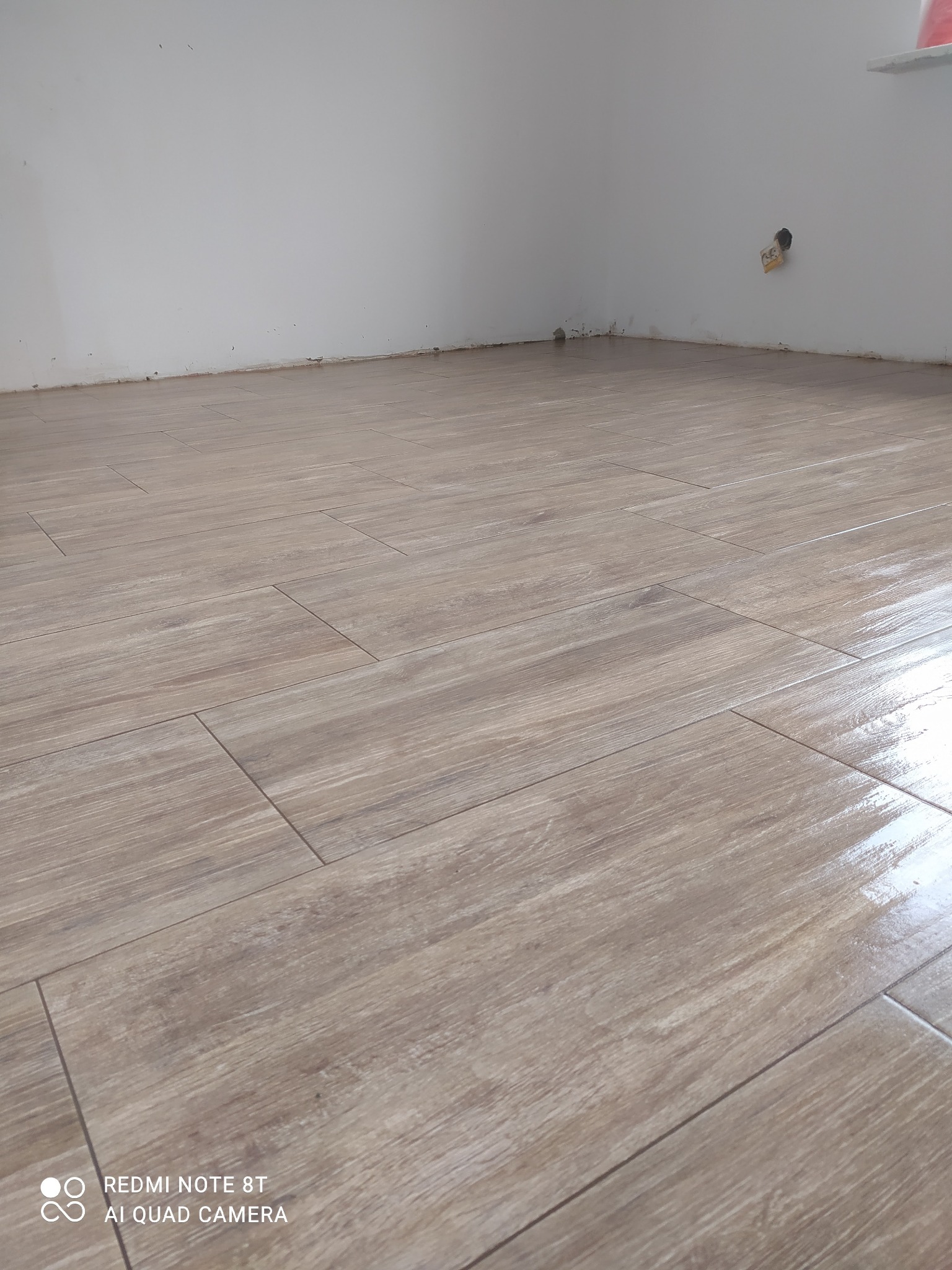 Ułożone, podłużne płytki podłogowe imitujące drewno, widoczne niedociągnięcia przy ścianie i wystająca instalacja elektryczna.