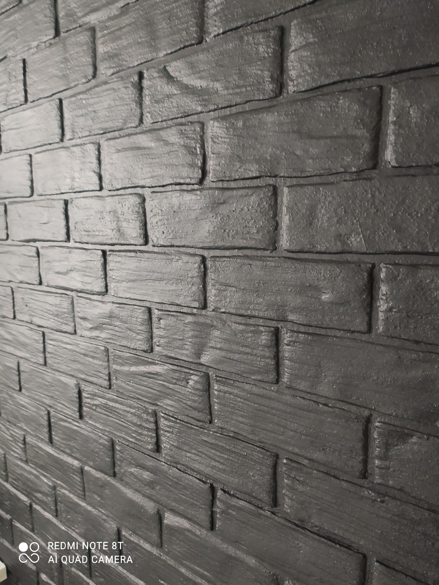 Ściana wykończona dekoracyjną, szarą cegłą z wyraźną fakturą drewna, imitacja starego muru, ujęcie pod kątem.