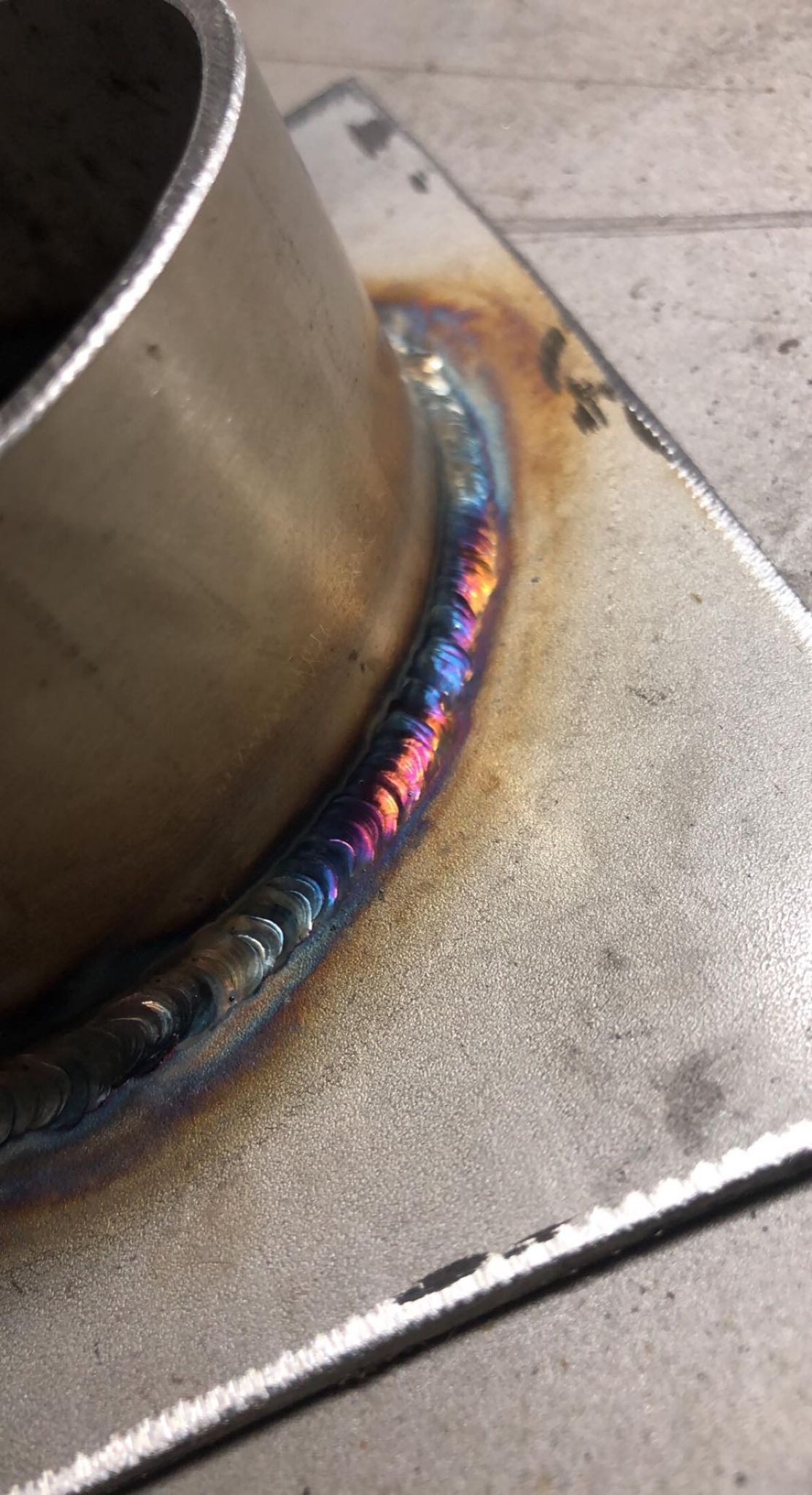 Połączenie spawane rury ze stalową płytą, widoczne opalizujące kolory na spoinie.