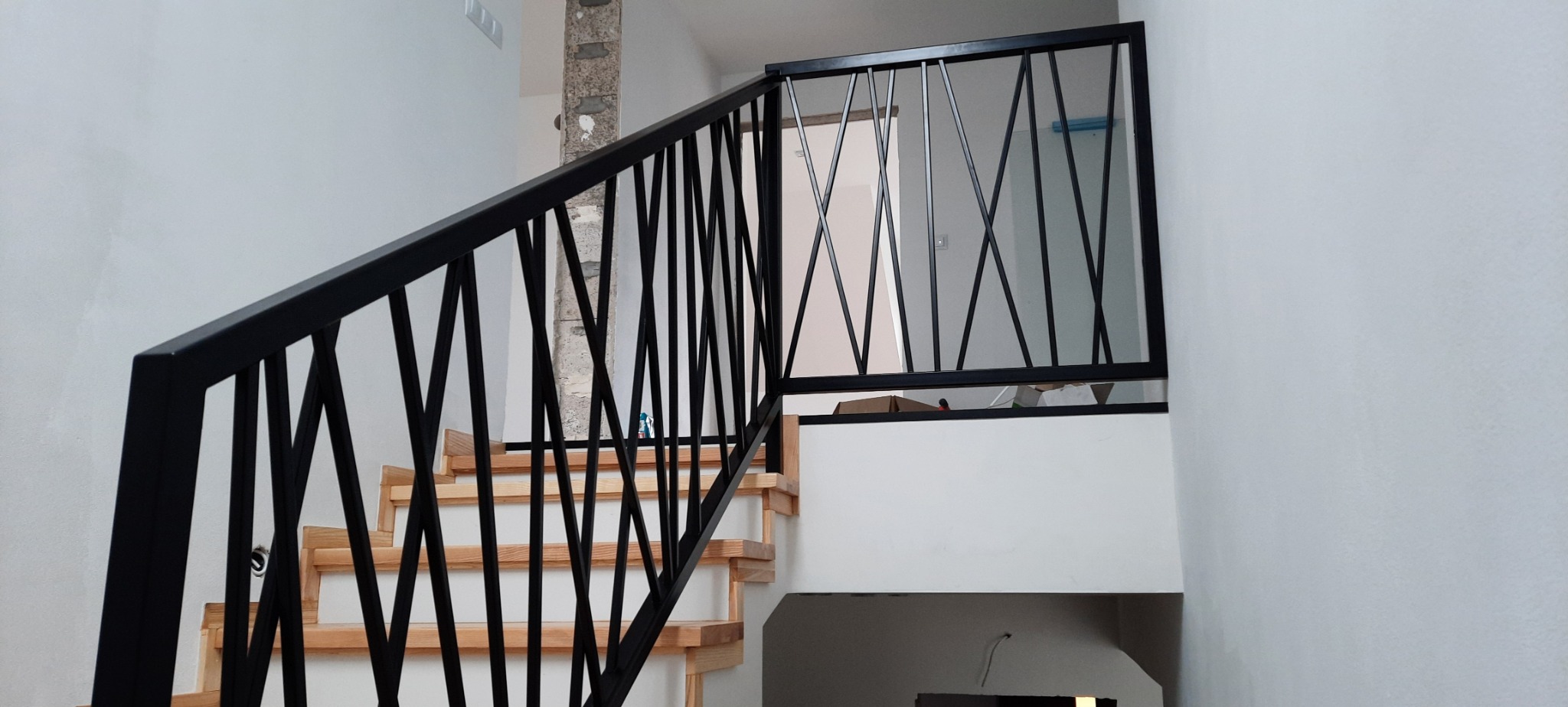 Schody drewniane z czarną, metalową balustradą o geometrycznym wzorze w nowoczesnym wnętrzu, widok z dołu.