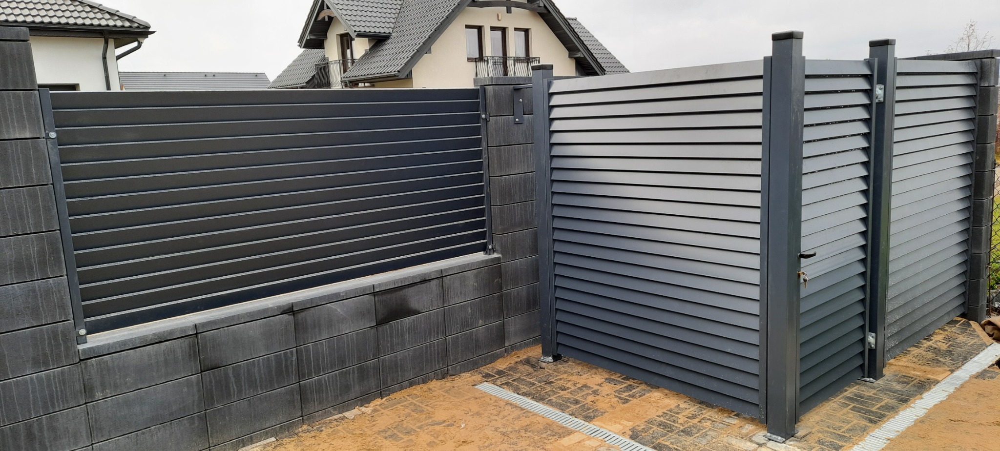 Nowoczesne, poziome, szare ogrodzenie z bramką na posesji w Siedliszczach, wykończone elementami z szarego betonu.