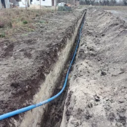 Wykop z niebieskim przewodem instalacyjnym w Grudziądzu, widok z góry na tle budowy i drzew.