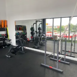 Wnętrze siłowni z rowerem stacjonarnym Rogue Echo Bike, lustrem odbijającym stojaki z obciążeniami i hantlami, oraz drabinkami gimnastycznymi z liną.