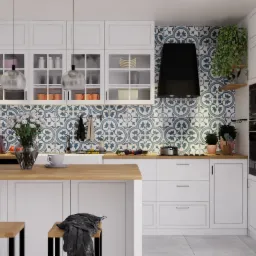 Nowoczesna kuchnia z białymi szafkami, drewnianym blatem, wzorzystą mozaiką na ścianie, czarnym okapem i roślinami doniczkowymi; widoczne wiszące lampy, czajnik i filiżanka.