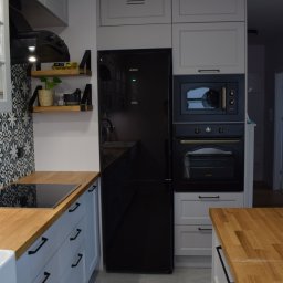 Vertical - Nowoczesna kuchnia z szarymi szafkami, drewnianym blatem i czarnym sprzętem AGD, w tym lodówką Hitachi i piekarnikiem Gorenje.