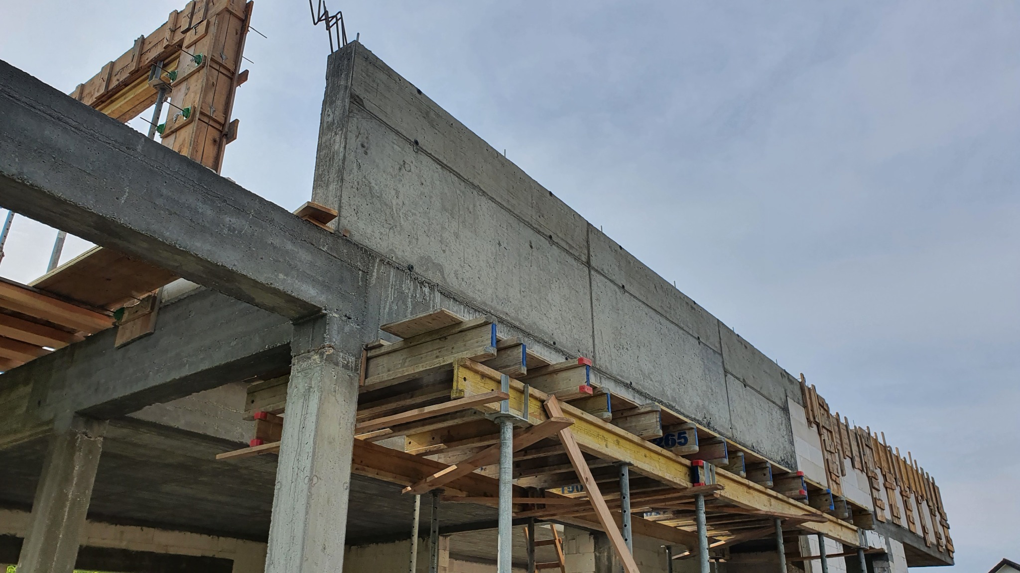 Wznoszenie budynku żelbetowego w Olsztynie: Szalunek i zbrojenie przygotowane do zalewania betonem, widoczne drewniane elementy konstrukcji i stalowe pręty zbrojeniowe.