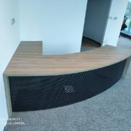 Recepcja z blatem drewnopodobnym i ażurowym frontem w nowoczesnym biurze, widoczna z niskiego kąta, z elementami wykończeniowymi w tle.