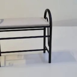 Czarny metalowy taboret z szarym tapicerowanym siedziskiem na białym tle, widok z boku.