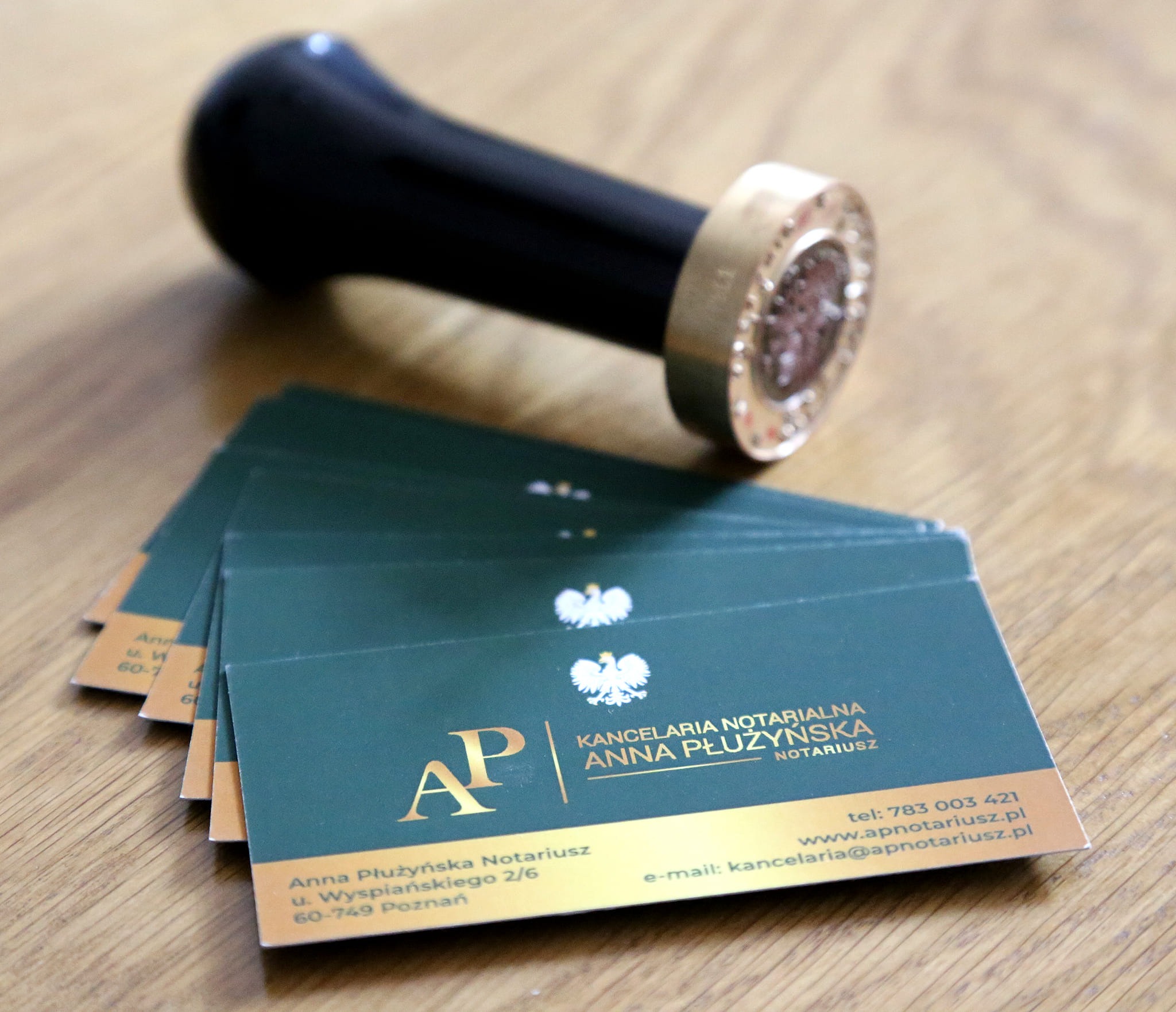 Stempel notarialny obok wizytówek Kancelarii Notarialnej Anny Płużyńskiej na drewnianym biurku.