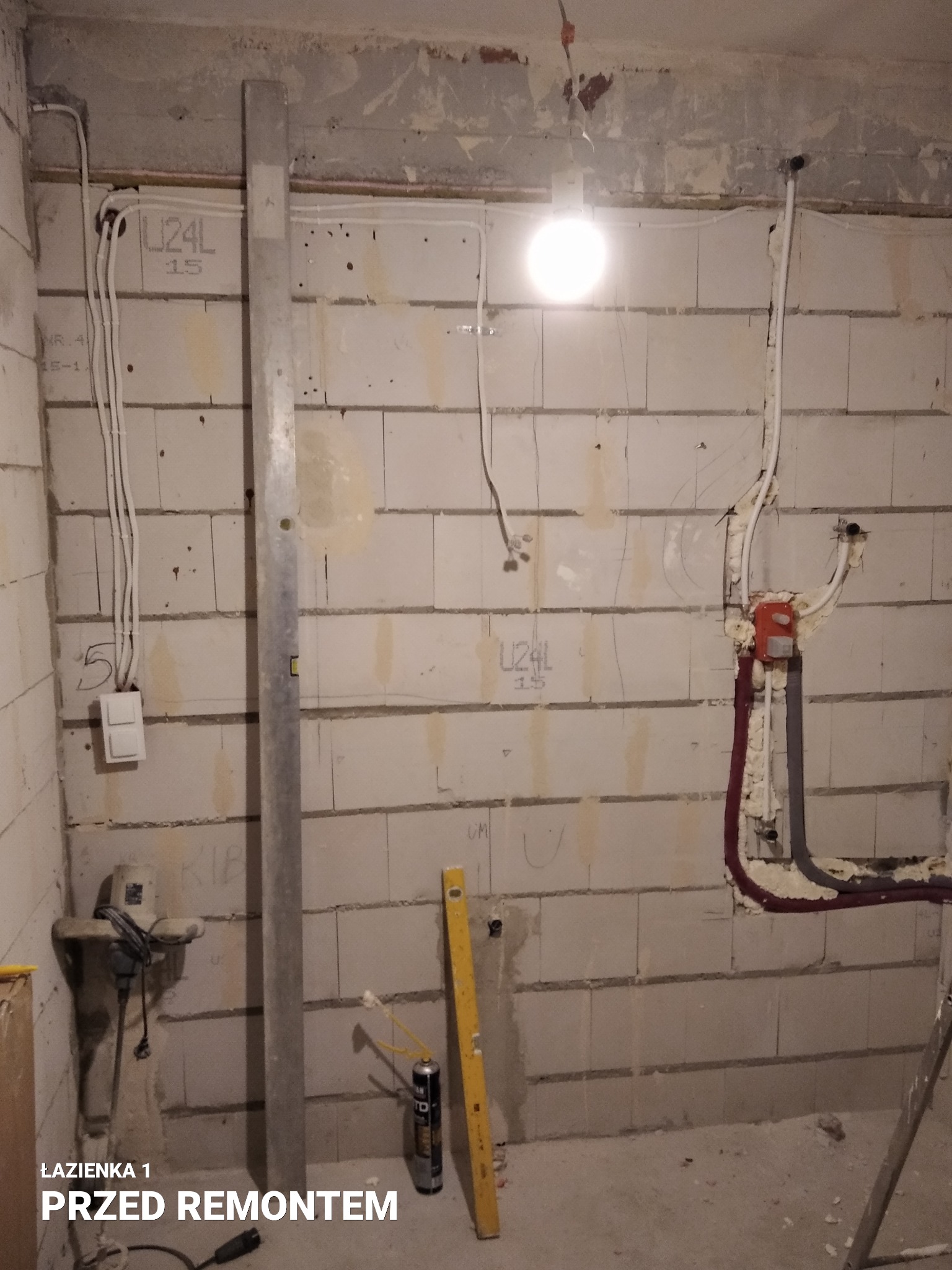Łazienka w trakcie przygotowań do remontu: widoczne instalacje elektryczne i hydrauliczne, ściany z betonu komórkowego z oznaczeniami, poziomica, narzędzia przygotowane do pracy.