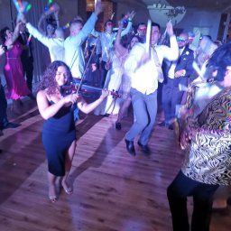 Kors&Relax - Skoczna zabawa z muzyką na żywo: skrzypaczka w czarnej sukience i saksofonista w wzorzystej marynarce, rozbawiony tłum z ledowymi pałeczkami w tle.