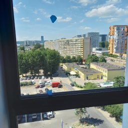 Sebuu - Widok z okna na panoramę miasta z blokami mieszkalnymi, parkingiem i fragmentem ulicy; na szybie okna przyklejone małe, niebieskie karteczki.