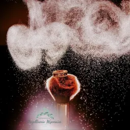 Pędzel do makijażu z pierścionkiem na włosiu, otoczony chmurą pudru na czarnym tle z efektem iskrzenia.