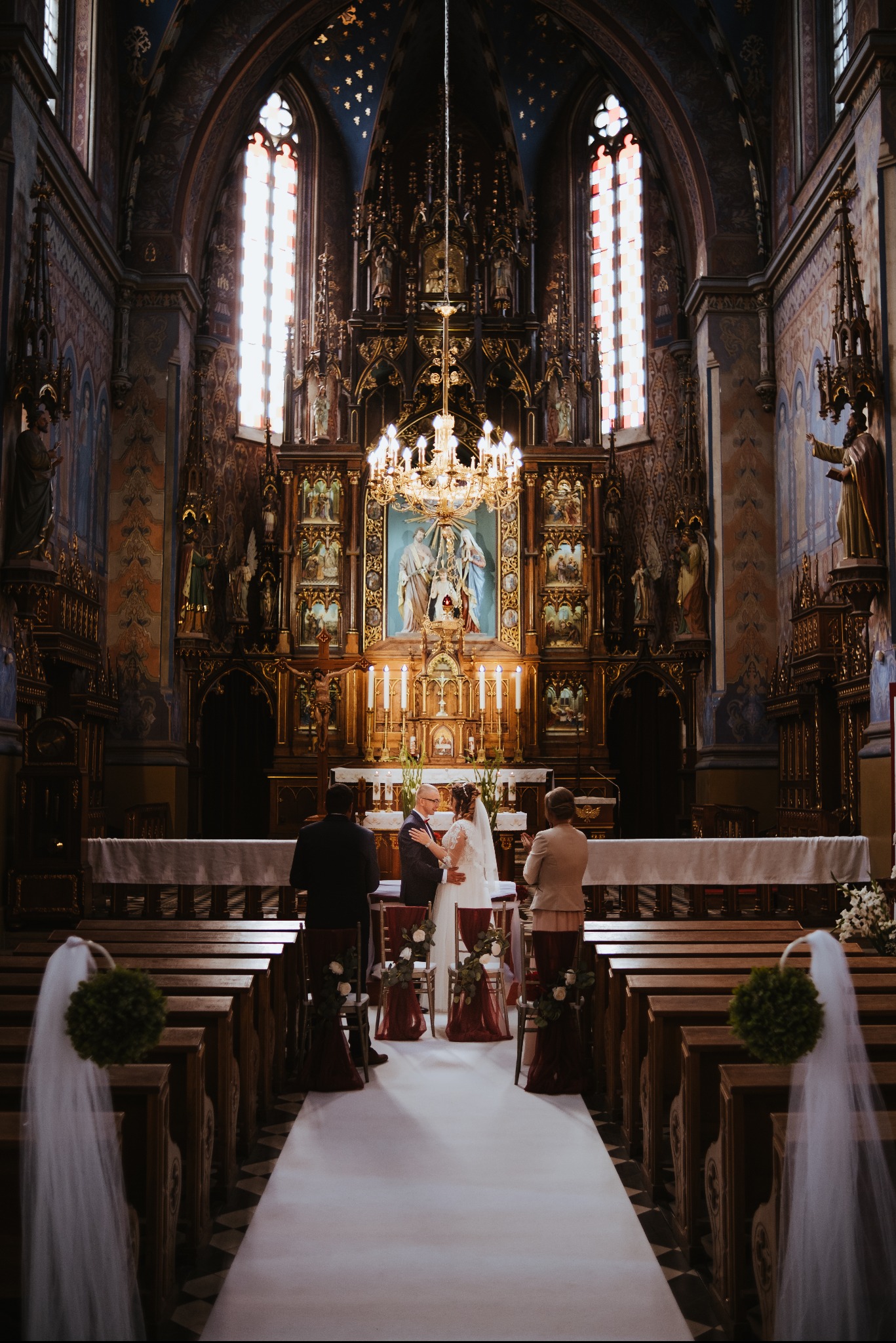 Para młoda podczas ceremonii ślubnej w bogato zdobionym kościele z wysokim ołtarzem i witrażami.