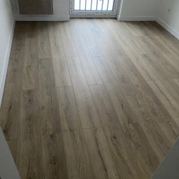 FORADEA SPÓŁKA Z OGRANICZONĄ ODPOWIEDZIALNOŚCIĄ - Jasne panele podłogowe z widoczną strukturą drewna w nowym pokoju z oknem balkonowym. Wykończenie w neutralnych odcieniach bieli i beżu. Minimalistyczny styl.